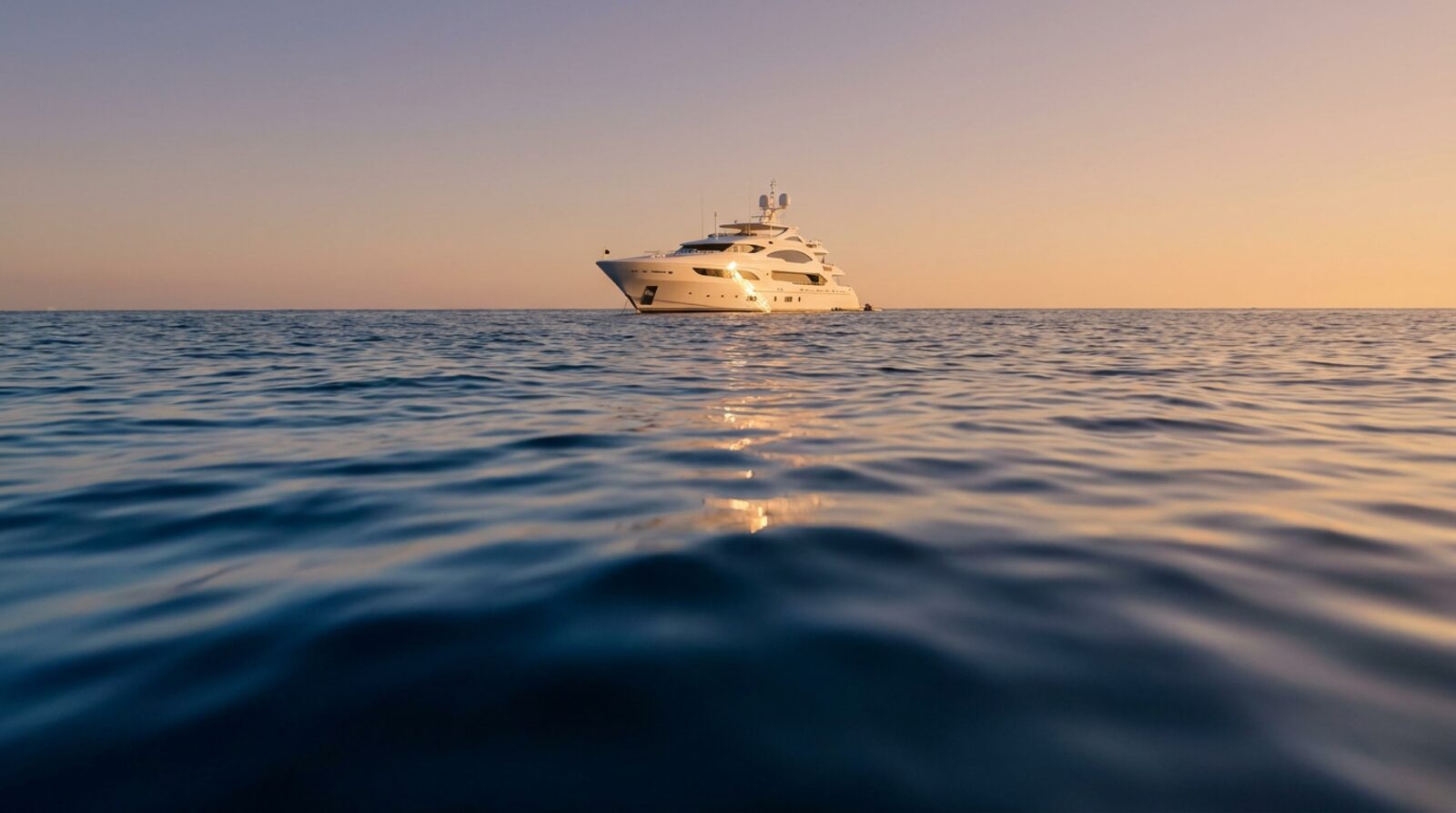 A white yacht moored on calm navy water at first light